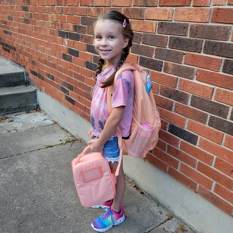 student smiling carrying her backpack and lunch box