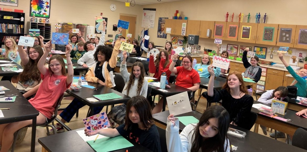 middle school art students hold up postcards